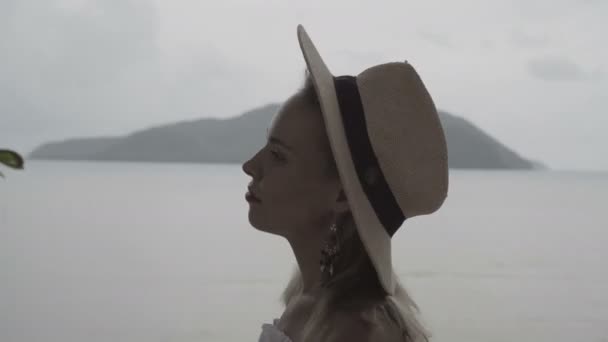 Vista a través de la ventana de la mujer de aspecto bastante natural en el día de verano en la moda de estilo boho con camisa blanca, bikini y sombrero caminando en una terraza sobre el hermoso paisaje marino de fondo . — Vídeo de stock