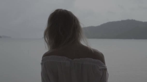 Retrato de close-up de mulher olhando muito naturalmente no dia de verão vestindo camisa branca boho e brincos tremendo cabelo em um terraço sobre belo fundo paisagem do mar - vídeo em câmera lenta . — Vídeo de Stock