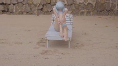 Modern fütüristik tarzı seksi güzel kadın Video hasarlı ahşap mavi şezlong üzerinde poz. Bikini ve mavi peruk giyen plajda kadının yaratıcı bir görünüm.
