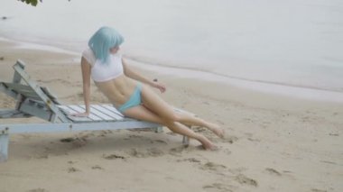 Modern fütüristik tarzı seksi güzel kadın Video hasarlı ahşap mavi şezlong üzerinde poz. Bikini ve mavi peruk giyen plajda kadının yaratıcı bir görünüm.