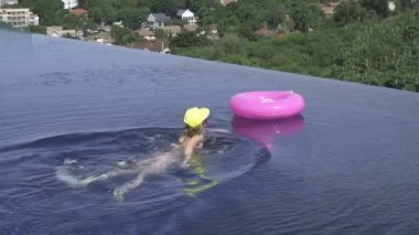 Bikini, sarı hat ve şişme ringde pembe: Infinity çatı havuzu ile güneşli bir günde yeşil ağaçlar peyzaj üzerinde Yüzme mor güneş gözlüğü giyen genç ve güzel kadın.