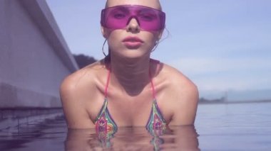 Seksi genç kadın kamera Infinity çatıdaki yüzme havuzunda güneşli bir günde mavi gökyüzü ve yeşil ağaçlar manzara bakan mor güneş gözlüğü takıyor yüz closeup.