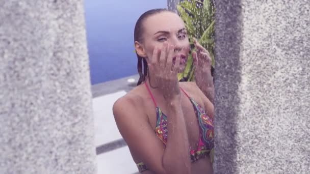 Cara de cerca de la sexy mujer rubia en bikini tomando una ducha al aire libre en la piscina rodeada de jardín tropical - video en cámara lenta . — Vídeos de Stock