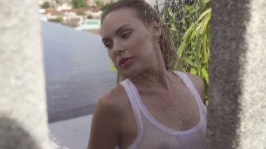 Bikinili ve beyaz atletli seksi sarışın kadın çatıda duş alıyor. Etrafı tropikal bahçelerle çevrili..