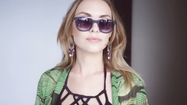 Glamour beautiful woman wearing black swimwear, floral long shirt and sunglasses walking out of ladys restroom - video in slow motion. — Stock Video