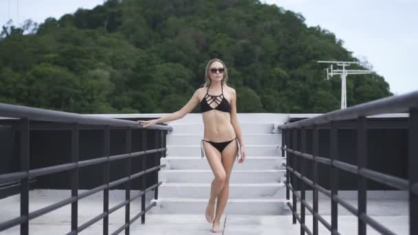 Sexy Blonde Glamour Woman Wearing Black Swimwear And Sunglasses Walking On A Rooftop In A Sunny Summer Day With Beautiful Sky And Green Mountain Landscape Sexy Blonde Glamour Woman Wearing Black Swimwear And Sunglasses Walking On A Rooftop In A Sunny Summer Day With Beautiful Sky And Green Mountain Landscape