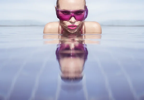 Face closeup of sexy young woman wearing purple sunglasses looking at camera in infinity rooftop swimming pool on a sunny day over blue sky and green trees landscape — Stock Photo, Image