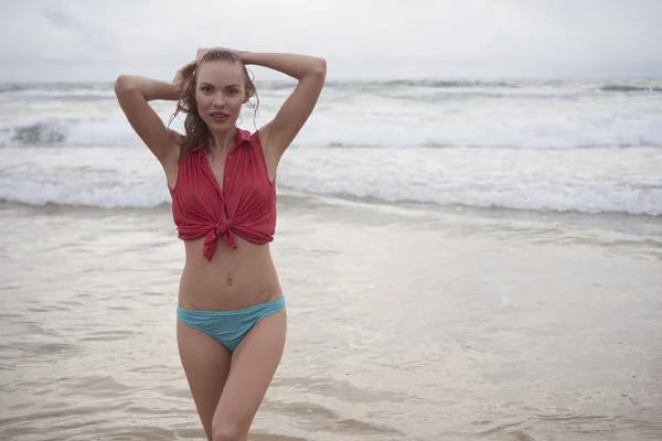 Mulher feliz loira bonita vestindo camisa de colarinho vermelho e fundo de biquíni azul posando em um belo dia de verão na praia sobre o fundo do mar e do céu — Fotografia de Stock