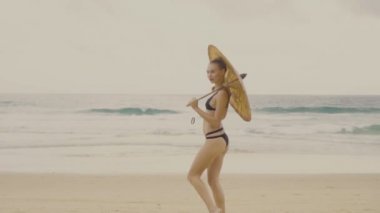 Güzel sarışın glamour kadın çin şemsiyesi gülümseyerek siyah mayo giyen ve plajda güzel bir yaz gününde poz - yavaş hareket video