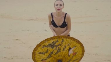 Güzel sarışın glamour kadın çin şemsiyesi gülümseyerek siyah mayo giyen ve plajda güzel bir yaz gününde poz - yavaş hareket video