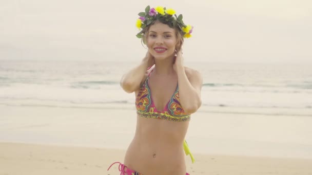 Hermosa mujer rubia glamour vistiendo trajes de baño de colores y corona sonriendo y posando en un hermoso día de verano en la playa sobre el mar y el fondo del cielo — Vídeo de stock