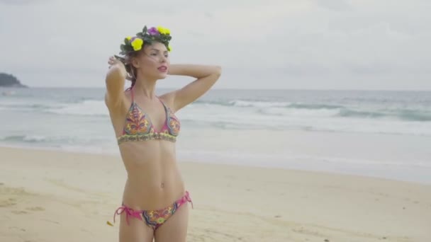 Mulher feliz loira bonita vestindo roupas de banho coloridas e grinalda sorrindo e posando em um belo dia de verão na praia sobre o fundo do mar e do céu — Vídeo de Stock