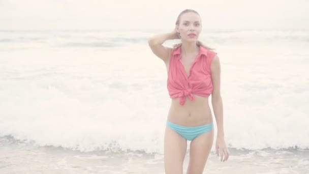 Mooie blonde gelukkige vrouw dragen rode kraag shirt en blauwe bikini bottom poseren op een mooie zomerdag op het strand over zee en hemel achtergrond-video in slow motion — Stockvideo