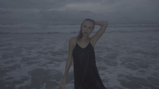 Schöne blonde Glamour-Frau in schwarzem Kleid posiert an einem Spätsommernachmittag am Strand mit nassen Haaren über Meer und Himmel — Stockvideo