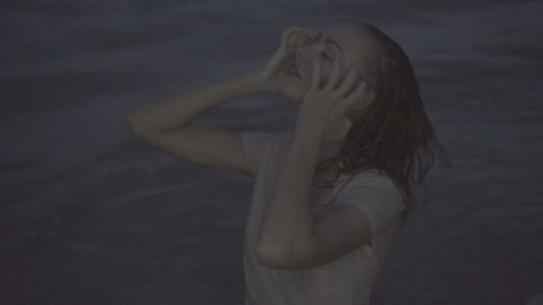 Блондинка в футболке, позирующая в море летним вечером с мокрыми волосами - видео в замедленной съемке — стоковое видео