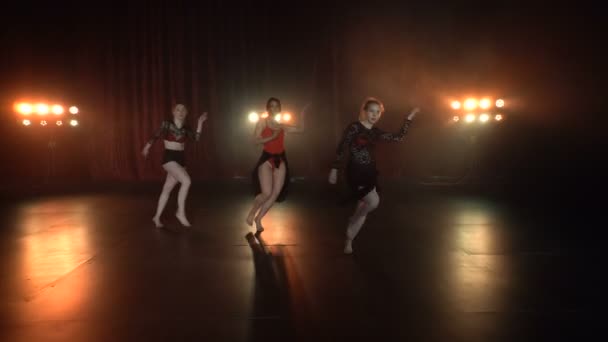 Danse performance de sexy groupe féminin sur une scène sombre avec des lumières orange et de la fumée — Video