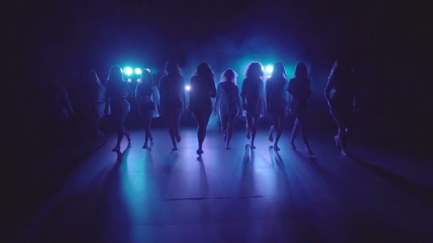 Shilouettes de bailarinas se agrupan sensualmente caminando sobre un escenario oscuro con luces y humo - video en cámara lenta — Vídeos de Stock