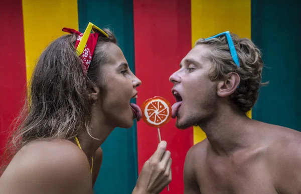 Divertido joven playa pareja lamiendo naranja lollipop juntos aislado colorido pared — Foto de Stock