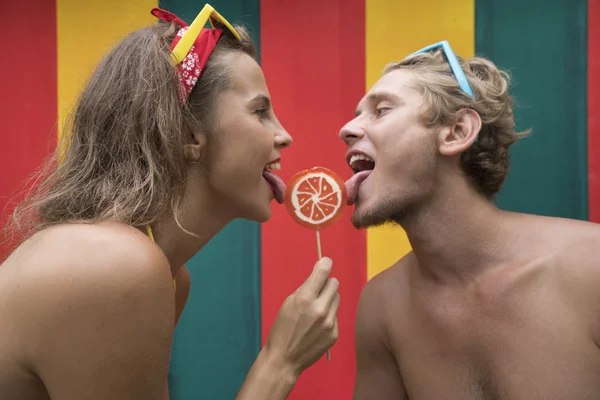 Divertido joven playa pareja lamiendo naranja lollipop juntos aislado colorido pared — Foto de Stock