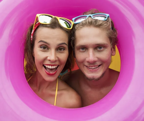 Divertido joven feliz playa pareja sonriendo aislado en el medio de rosa anillo inflable — Foto de Stock