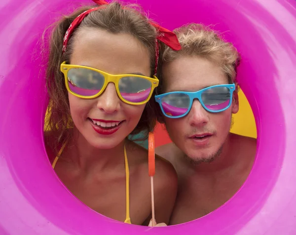 재미있는 젊고 행복 한 해변 부부가 분홍색부풀어 오르는 반지 한 가운데서 미소짓고 있다 — 스톡 사진