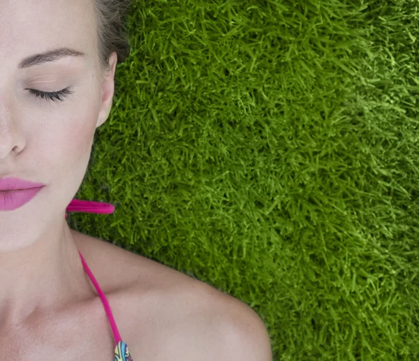 Close-up van vrij half gezicht vrouw het dragen van bikini liggend op een groen gras op een zonnige dag — Stockfoto