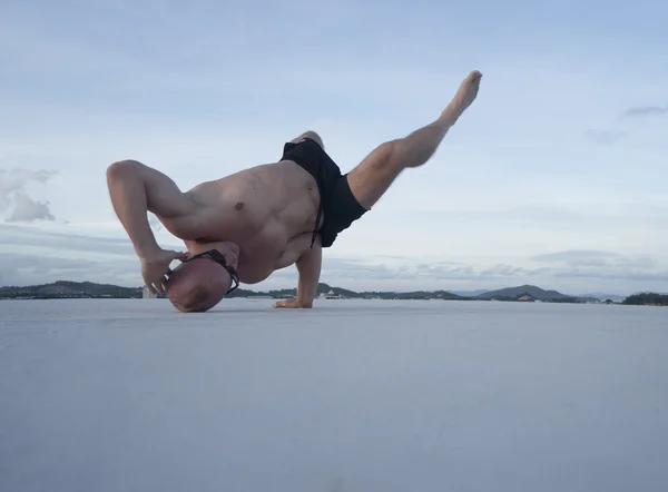 Bonito jovem com tronco nu e óculos de sol fazendo movimentos de dança de freio em um telhado sobre o fundo do céu — Fotografia de Stock