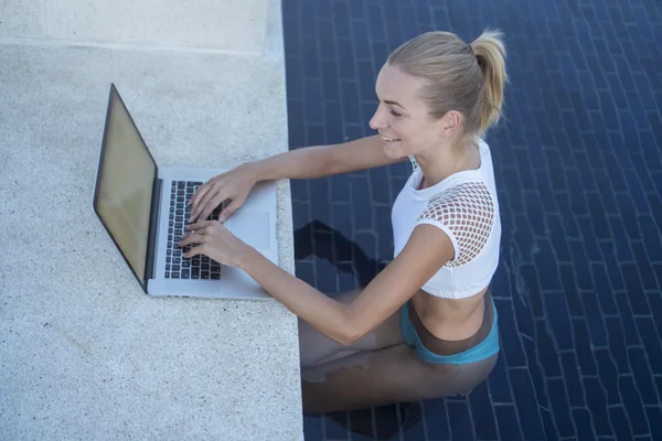 Outdoors portrait of pretty blonde happy woman in bikini with laptop computer in a rooftop swimming pool. Freelance and technology — Stock Photo, Image