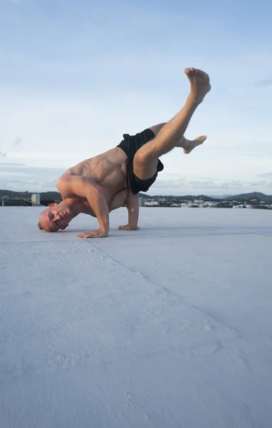 Bonito jovem com tronco nu e óculos de sol fazendo movimentos de dança de freio em um telhado sobre o fundo do céu — Fotografia de Stock