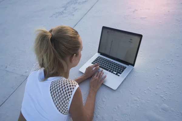 Back top view of pretty blonde woman in white top with laptop computer lying on a rooftop. Freelance and technology — Stock Photo, Image