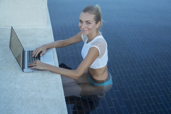 Outdoors portrait of pretty blonde happy woman in bikini with laptop computer in a rooftop swimming pool. Freelance and technology — Stock Photo, Image