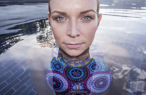 Face closeup de mulher loira bonita com belos olhos azuis vestindo trajes de banho coloridos olhando para a câmera na piscina no terraço em um dia ensolarado — Fotografia de Stock