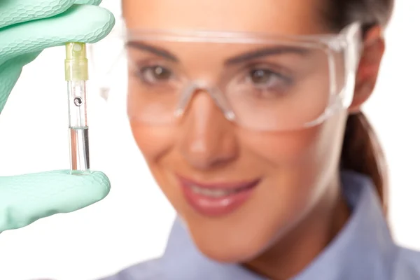Técnica de laboratório feminina atraente examinando um tubo de ensaio que ela está segurando em sua mão com foco seletivo para o tubo de ensaio isolado em branco — Fotografia de Stock