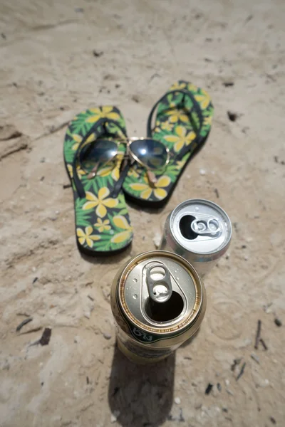 Vista superior de chinelos, óculos de sol e latas de bebidas em uma praia de areia oceânica. Conceito férias de verão — Fotografia de Stock