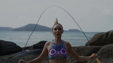 Güzel sarışın kadın kullanarak yaz gündüzleri deniz kenarında kayalar arasında ip atlama egzersiz