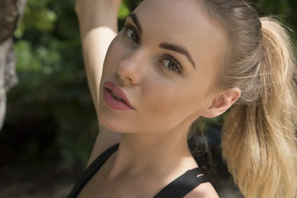 Closeup portrait of a beautiful blonde woman between trees on a beach during beautiful summer day — Stock Photo, Image