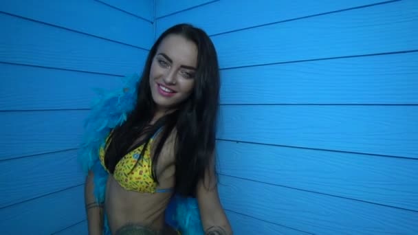 Bela mulher sedutora sorrindo e dançando usando biquíni amarelo e pluma azul boa sobre fundo de parede azul — Vídeo de Stock