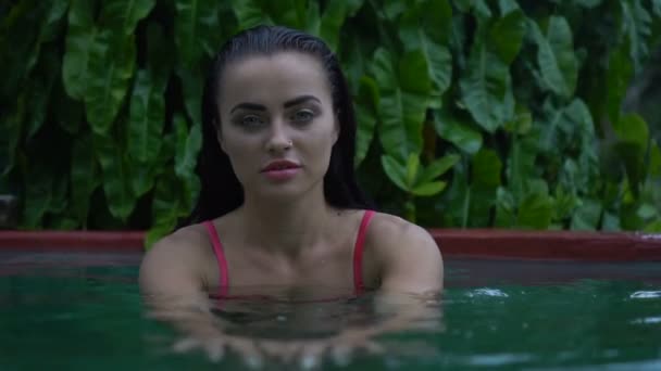 Retrato de cerca de una hermosa morena sexy con bikini rosa relajándose en la piscina al aire libre en el resort tropical — Vídeos de Stock
