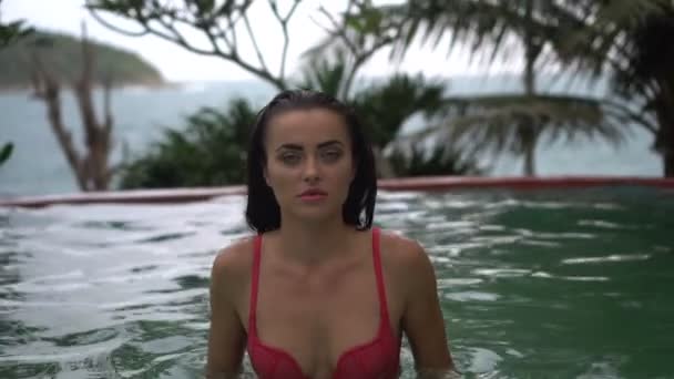 Hermosa mujer morena sexy con bikini rosa relajándose en la piscina al aire libre en el complejo tropical — Vídeos de Stock