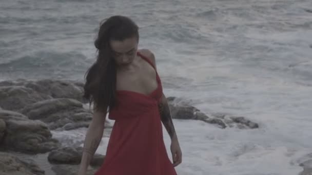 Bella donna seducente in abito rosso che si diverte sulle rocce in riva al mare — Video Stock