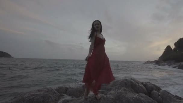 빨간 옷을 입은 아름다운 매력적 인 여자 가 바닷가 바위 위에서 즐기고 있다 — 비디오
