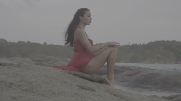 Güzel, baştan çıkarıcı, kırmızı elbiseli kadın deniz kenarındaki kayalıklarda eğleniyor. — Stok video