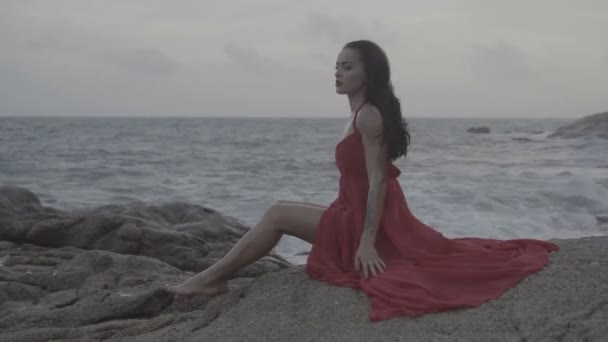 Bela mulher sedutora em vestido vermelho se divertindo em rochas junto ao mar — Vídeo de Stock