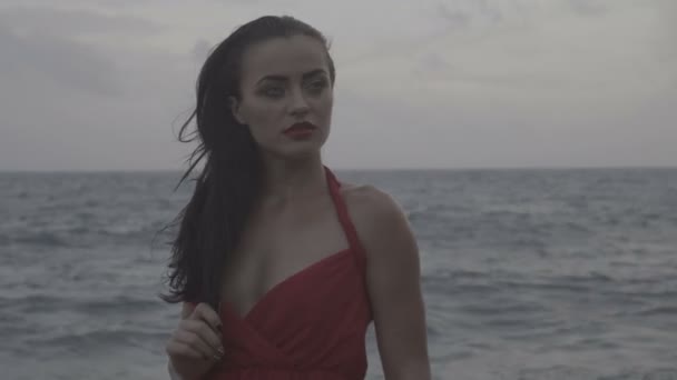 Bella donna seducente in abito rosso che si diverte sulle rocce in riva al mare — Video Stock