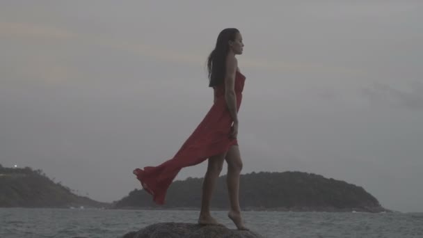 Bella donna seducente in abito rosso che si diverte sulle rocce in riva al mare — Video Stock