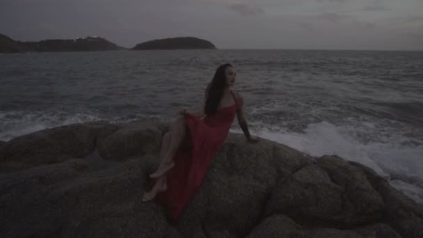 Bella donna seducente in abito rosso che si diverte sulle rocce in riva al mare — Video Stock