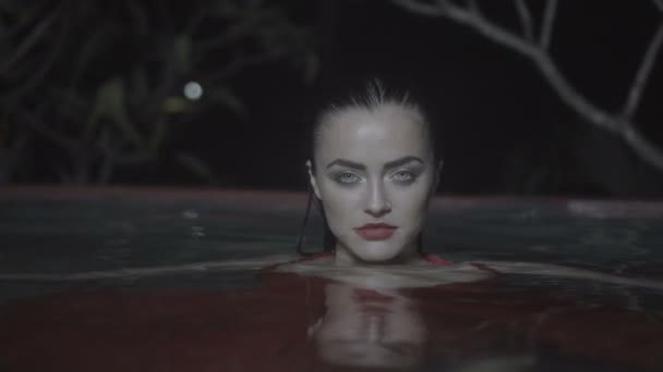 Belle femme séduisante portant une robe rouge dans la piscine extérieure la nuit — Video