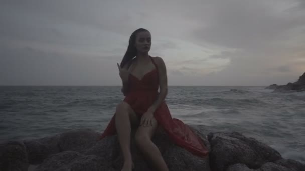 Hermosa mujer seductora en vestido rojo disfrutando en las rocas junto al mar — Vídeo de stock