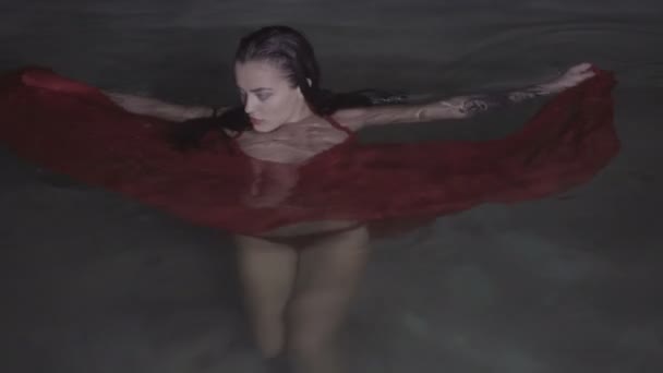 Красива спокуслива жінка в червоній сукні у відкритому басейні вночі — стокове відео