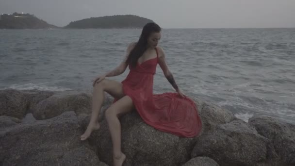 Bela mulher sedutora em vestido vermelho se divertindo em rochas junto ao mar — Vídeo de Stock